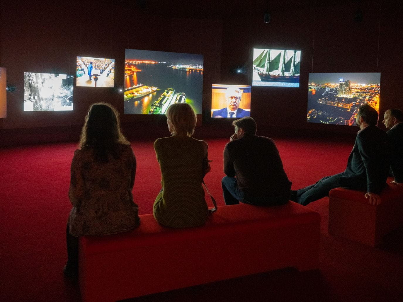 People at a multi media installation watching images on 6 different screens.